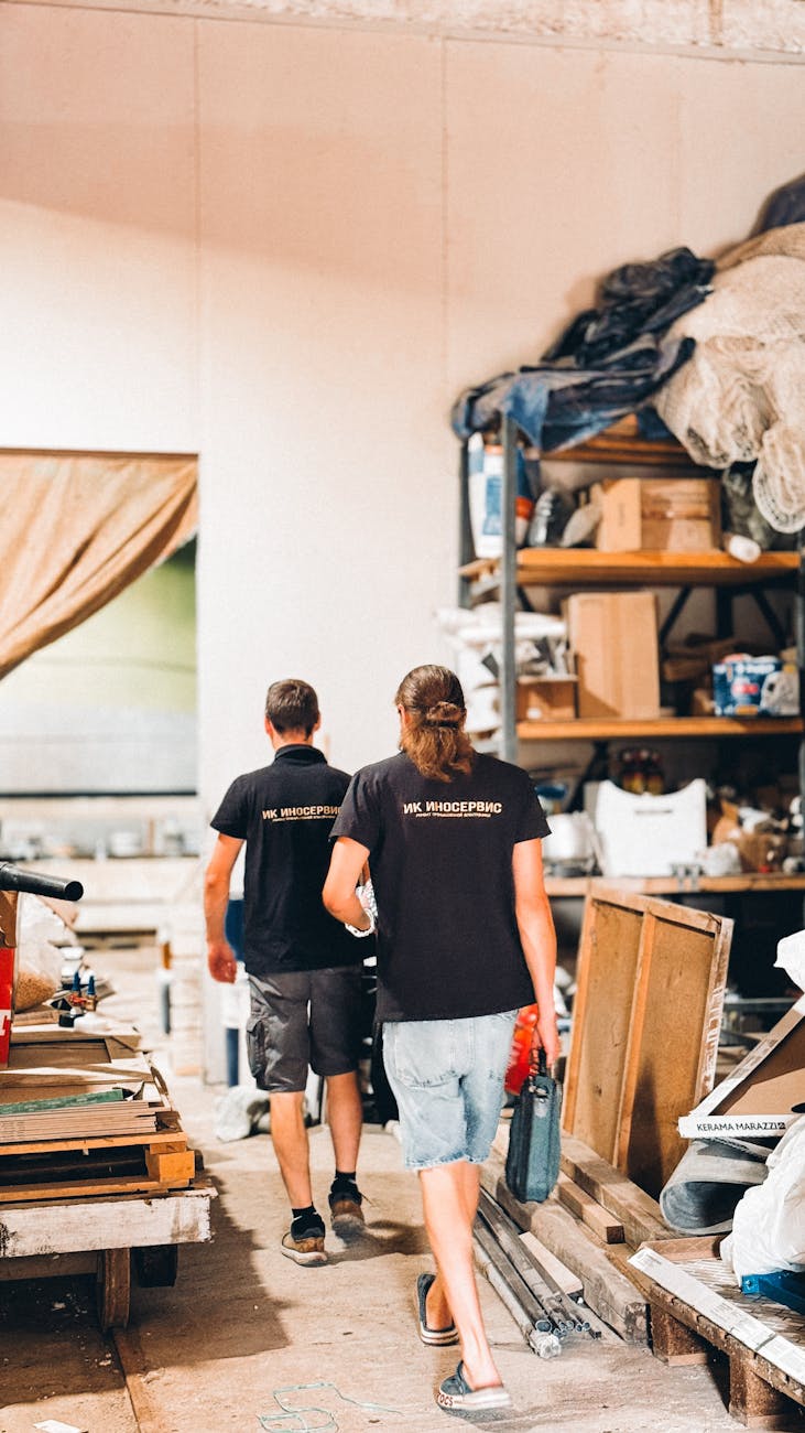 Two male workers in a workshop full of tools and materials, creating a busy industrial scene.