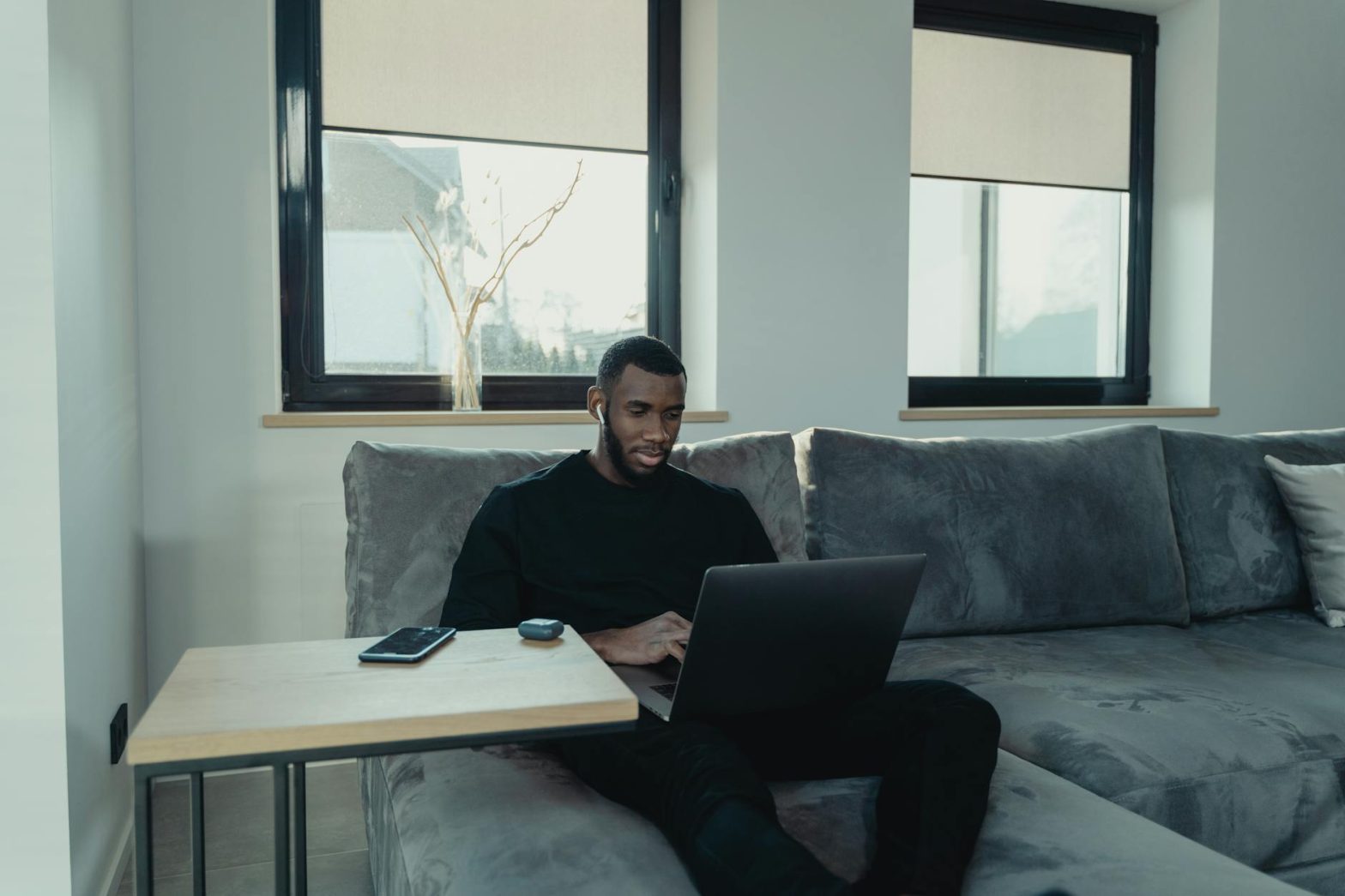 Man sitting on a sofa working on a laptop from home, with a cozy and modern interior setting.