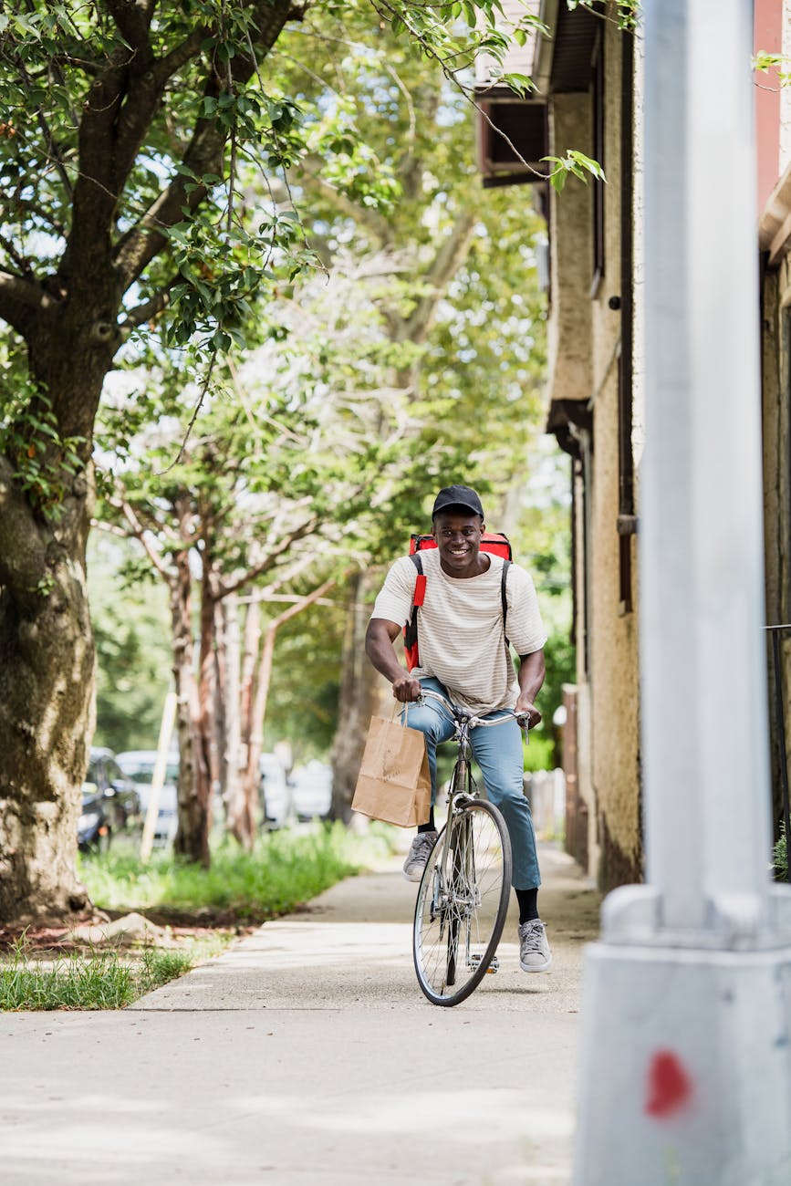 Smiling courier riding a bicycle on a sunny day delivering a package in the city.