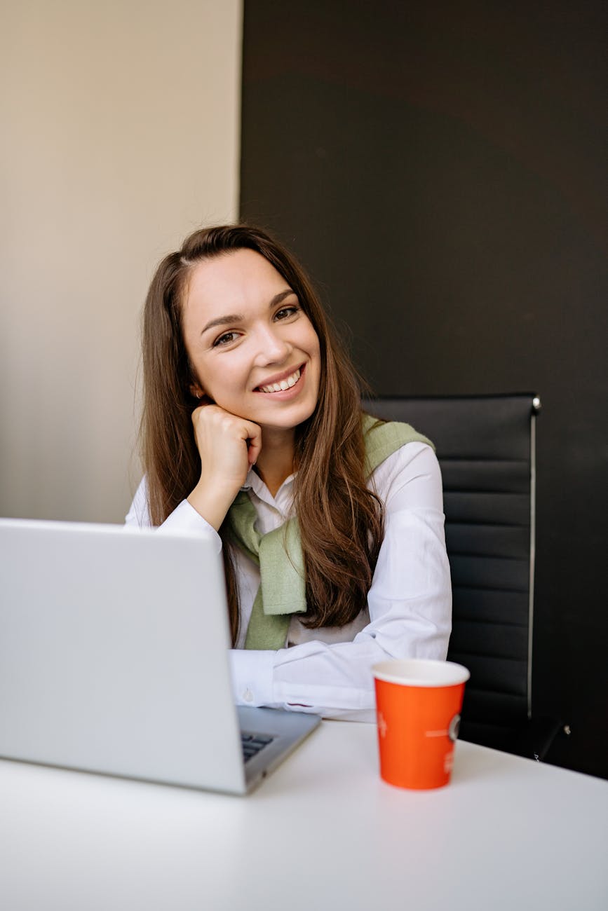 Confident woman with laptop and coffee smiling in a stylish office environment.
