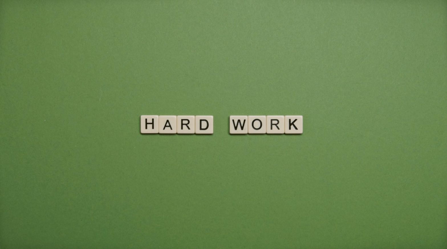 Tiles spelling 'hard work' on a green background symbolizing diligence and effort.