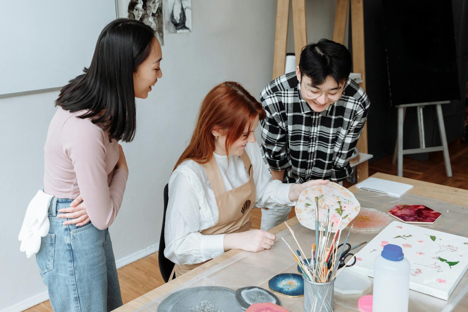 Three adults engaging in artistic activities in a bright art studio setting.