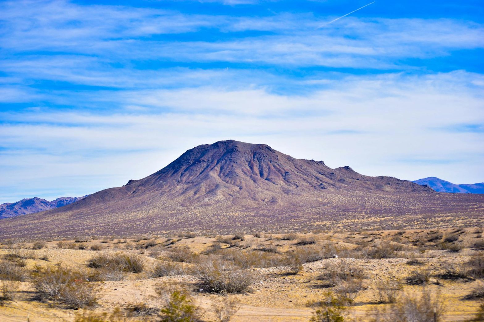 A striking mountain in the arid desert landscape of Nevada under a vast blue sky.