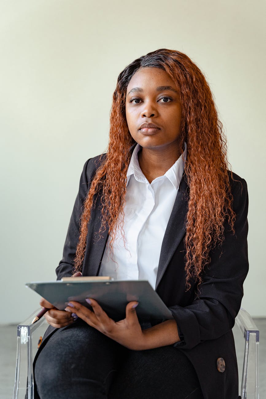 A pensive mental health professional sits holding a clipboard, prepared for a session.