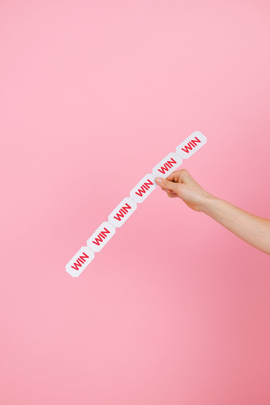 Conceptual image of a hand holding 'WIN' labels against pink background.