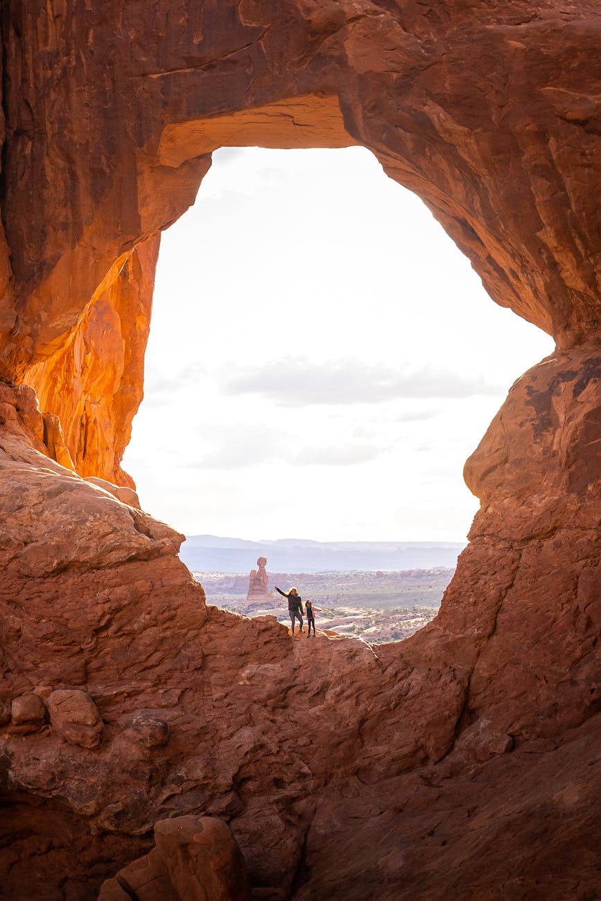 Hikers explore a sunlit natural arch in the stunning Arches National Park.