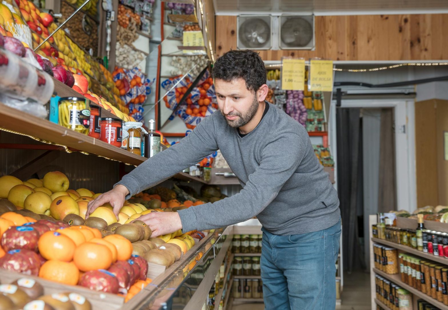 Grocery store worker organizing fresh fruits and vegetables on display shelves.