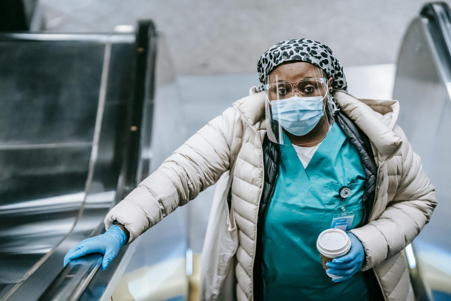 A healthcare worker wearing protective gear on an escalator in a subway station.