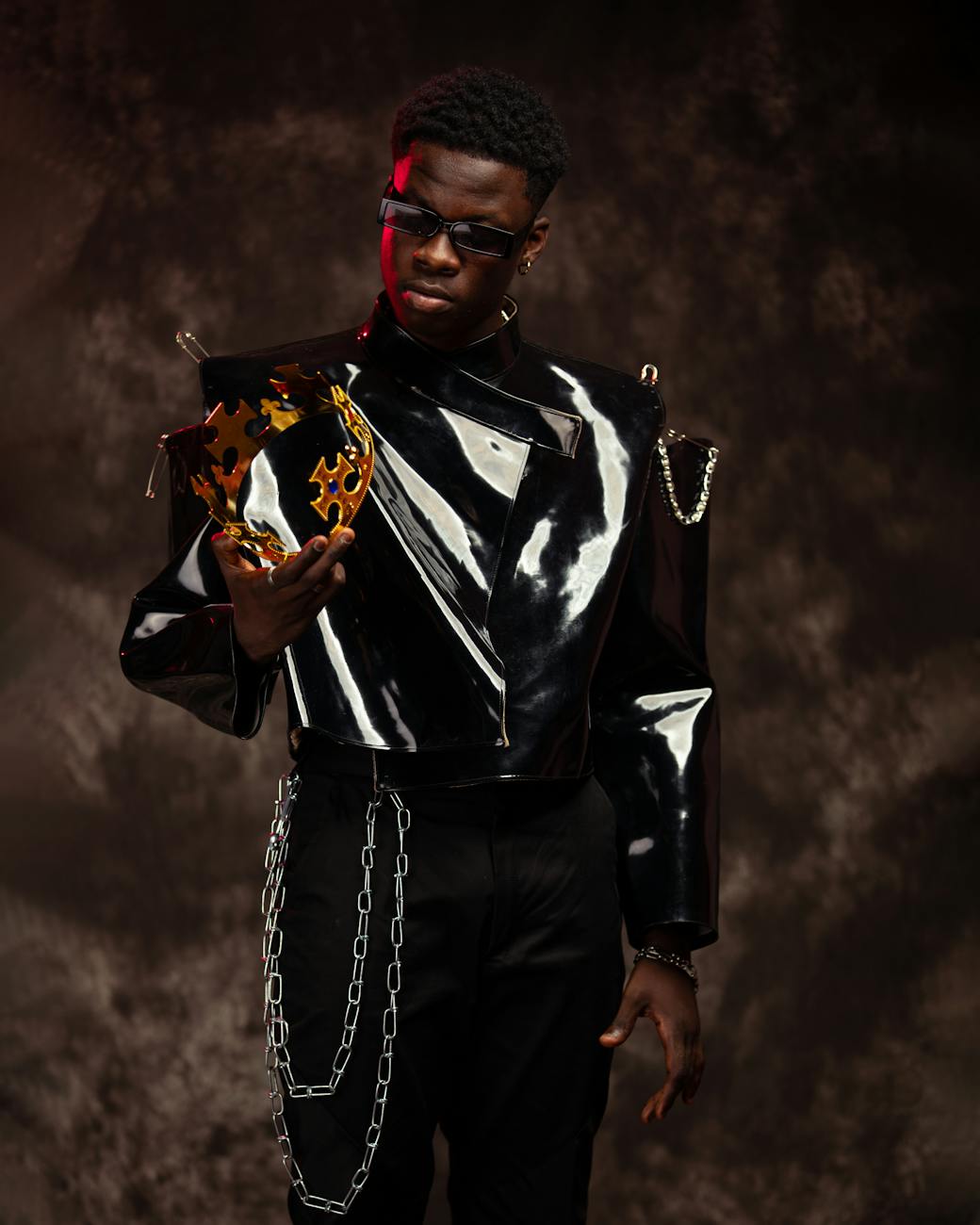 Fashionable portrait of a model in a black leather jacket, holding a unique metallic crown during a studio shoot.