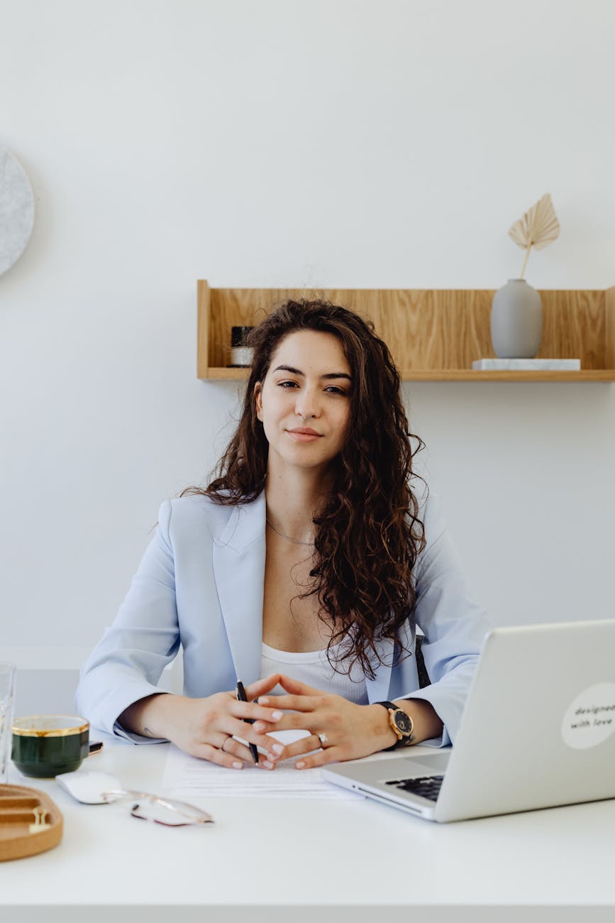 Portrait of a confident businesswoman sitting at a desk with a laptop in a modern office.