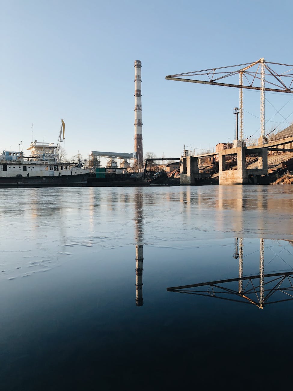 A serene industrial harbor scene in Kyiv, reflecting structures on calm waters at dawn.